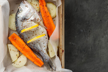 Fresh raw dorado fish with vegetables and lemon slices on baking sheet. Top view. Copy space