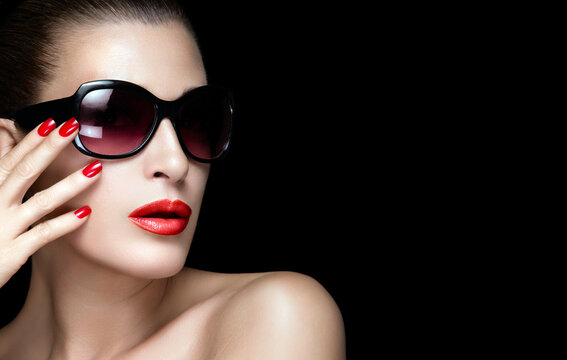 Beauty, fashion, and glamour. Elegant young woman wearing red lipstick and sunglasses in close-up portrait isolated on black background.