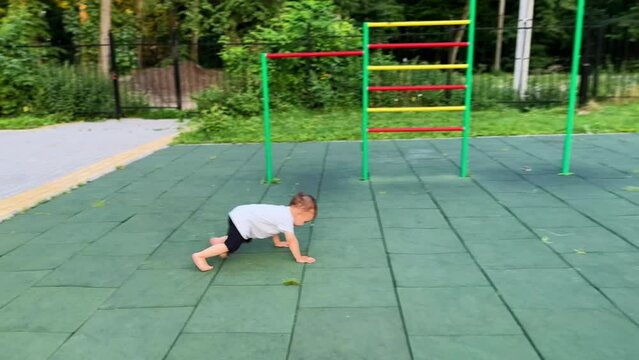 Baby boy running by the playground, trips and falls down. Kid stands up and goes to the ladder.