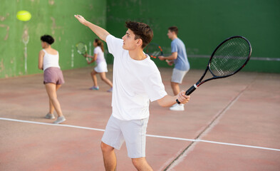Caucasian young man serving ball during frontenis game outdoors. Boy playing pelota on outdoor fronton.