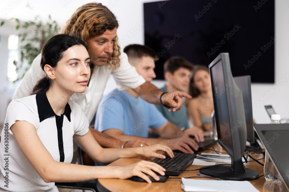 Wall mural Interested young girl attending computer class, learning digital technology under guidance of positive adult male teacher standing nearby..