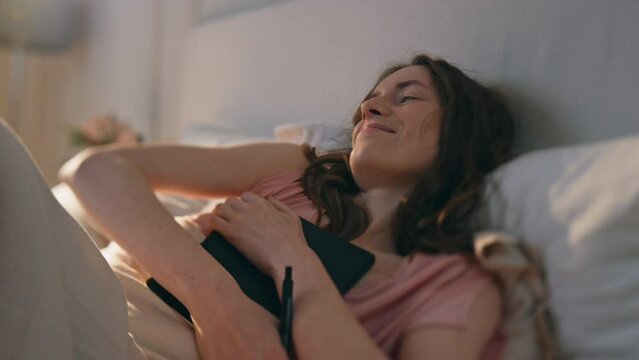 Peaceful girl holding diary in bed closeup. Smiling happy woman closing book