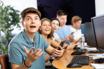 Fototapeta premium With his smartphone, young man remains engaged in auditorium during lesson