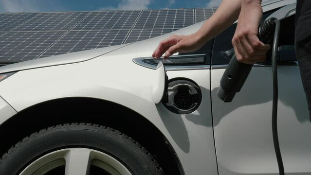 Male hands disconnect power cable supply to charge EV or electric car on the solar panels background. Unrecognizable man unplug an electric auto or PHEV at photovoltaic charging station