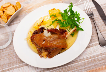 Just cooked portion of duck confit with fried poatoes served on table with serving pieces.