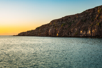 Fototapeta na wymiar Autumn Sunset over Espíritu Santo: Calm Waters and Rugged Cliffs