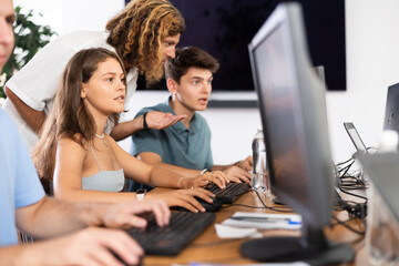 Enthusiastic young girl studying in computer lab with fellow students engrossed in coursework....