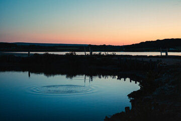 A pebble creates a splash of water in a lake at twilight
