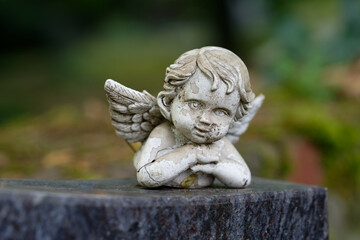 small damaged and weathered putto figure with wings lies on a tombstone