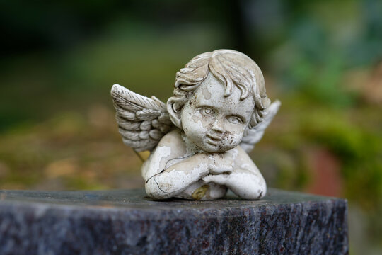 small damaged and weathered putto figure with wings lies on a tombstone