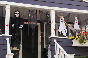 Halloween decorations adorn a haunted house front yard, featuring pumpkins, ghosts, and cobwebs, creating a spooky and festive atmosphere