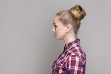 Side view portrait of serious self-confident woman with bun hairstyle standing looking ahead with...