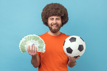 Portrait of happy smiling man with Afro hairstyle wearing orange T-shirt holding soccer ball and...