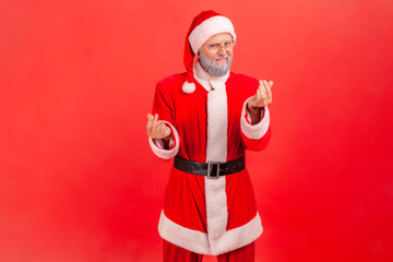 Portrait of positive elderly man with gray beard wearing santa claus costume making money gesture,...