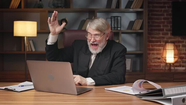 Happy aged businessman in formal suit rejoicing at work results on portable computer in modern office. Overjoyed professional employee getting excited about great news received via email account.