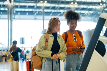Woman friends using self Check-in kiosk machine getting airline ticket boarding pass in airport terminal. People travel with using technology on holiday vacation and airplane transportation concept.