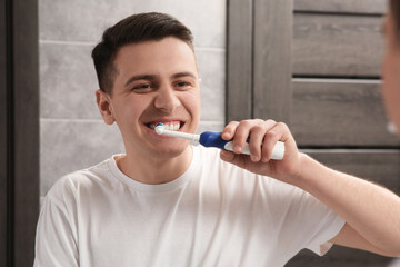 Man brushing his teeth with electric toothbrush in bathroom