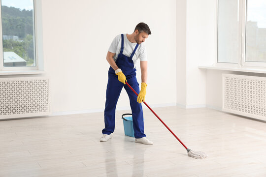 Man in uniform cleaning floor with mop indoors
