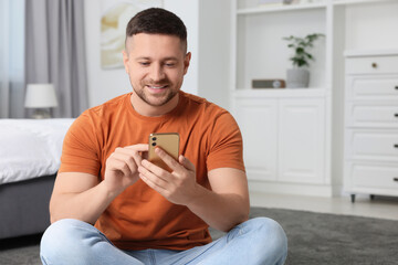 Handsome man sending message via smartphone at home. Space for text