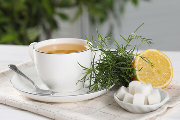 Aromatic herbal tea, fresh tarragon sprigs, sugar cubes and lemon on white table, closeup