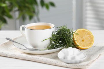 Aromatic herbal tea, fresh tarragon sprigs, sugar cubes and lemon on white wooden table
