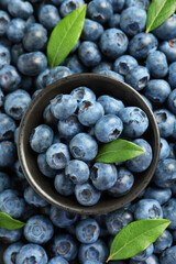 Tasty fresh blueberries with green leaves and bowl, top view
