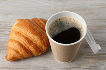 Coffee to go. Paper cup with tasty drink and croissant on white wooden table, closeup