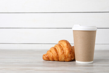 Coffee to go. Paper cup with tasty drink and croissant on white wooden table. Space for text