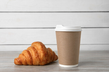 Coffee to go. Paper cup with tasty drink and croissant on white wooden table