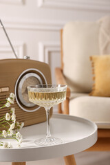 Glass of alcohol drink, flowers and radio set on table in room, closeup. Relax at home