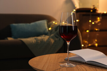 Glass of red wine and open notebook on wooden table in room, space for text. Relax at home