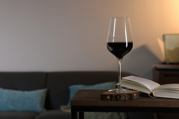 Glass of red wine and open book on wooden table in room, space for text. Relax at home