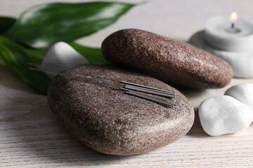 Stones with acupuncture needles on white wooden table, closeup