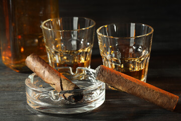 Cigars, ashtray and whiskey on black wooden table, closeup