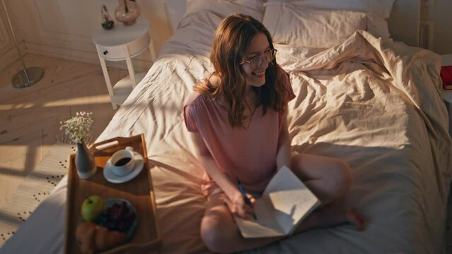 Smiling girl writing book in morning. Inspired carefree woman enjoying free time