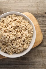 Tasty boiled oatmeal in bowl on wooden table, top view