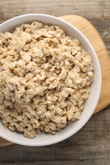 Tasty boiled oatmeal in bowl on wooden table, top view