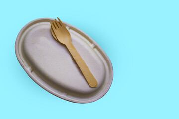 Compostable oval paper plate and wooden fork isolated on blue background. Eco friendly concept.
