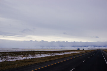 Beautiful winter landscape with a highway between blue snowy mountains, fluffy clouds on a sunset orange sky. Winter snow background. Elk Mountain, Wyoming, USA. Picturesque winter sky