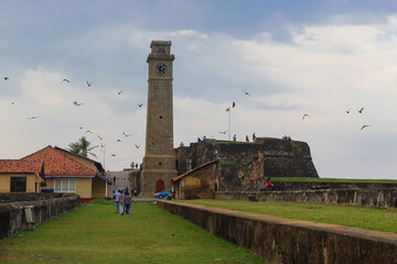 Fototapeta na wymiar Birds flying over the old clock tower at Galle Dutch Fort 17th Century