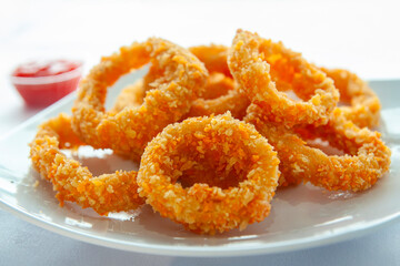Onion rings are placed on a white plate with spicy sauce on an isolated white background
