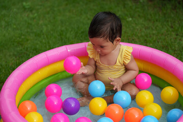 Fototapeta na wymiar infant baby girl playing water with colorful plastic balls in inflatable pool