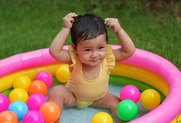 Obraz premium happy infant baby girl playing water with colorful plastic balls in inflatable pool