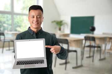 Portrait of male Asian teacher with laptop in classroom