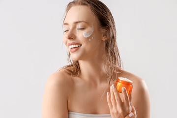 Pretty young woman with facial cream on light background