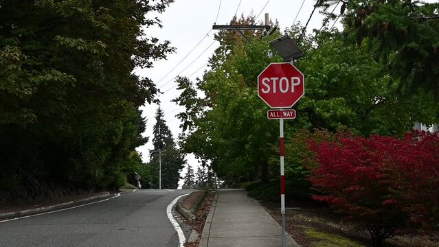 Blinking 4 way stop sign powered a solar panel in a residential neighborhood