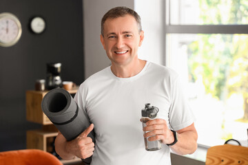 Sporty mature man with bottle of water and fitness mat at home