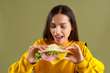 Female student with tasty sandwich on green background