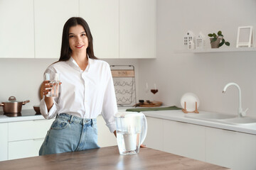 Young woman with glass and water filter jug in kitchen