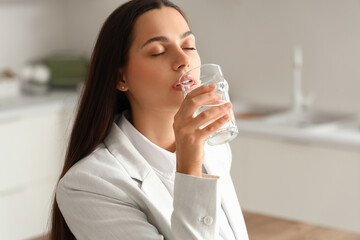 Beautiful young woman with drinking water in kitchen